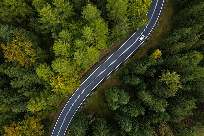 鸟瞰图，一辆汽车行驶在弯曲的道路上，穿过周围的绿色森林